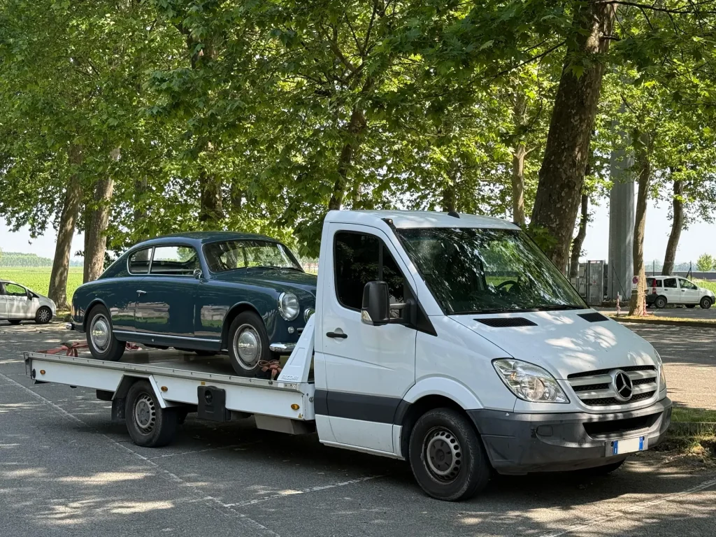 Bisarca Mercedes Sprinter di Rubino Express con Lancia Aurelia B20 GT verde petrolio caricata, in sosta in un parcheggio alberato